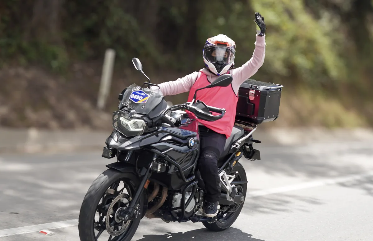 Una motociclista con chaleco rosa saluda durante el recorrido